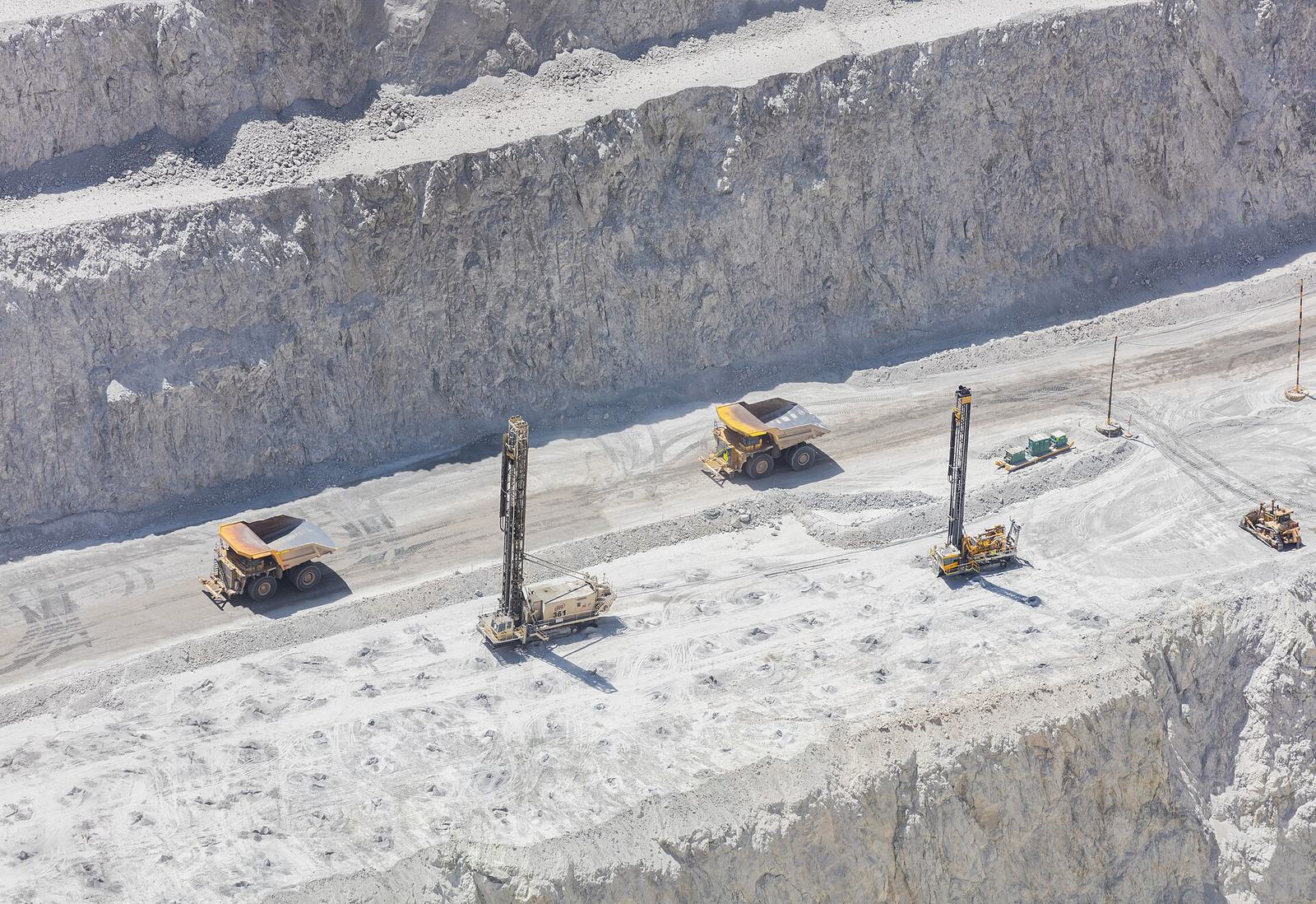 Haul trucks and drill rigs on a pale bench of the Chuquicamata pit