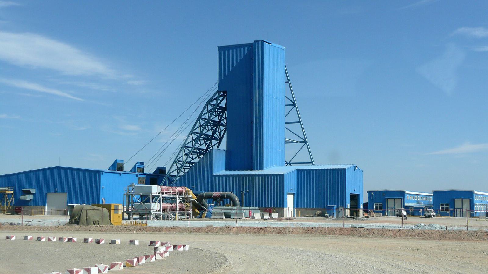 A tall blue shaft headframe and plant buildings in the Gobi desert