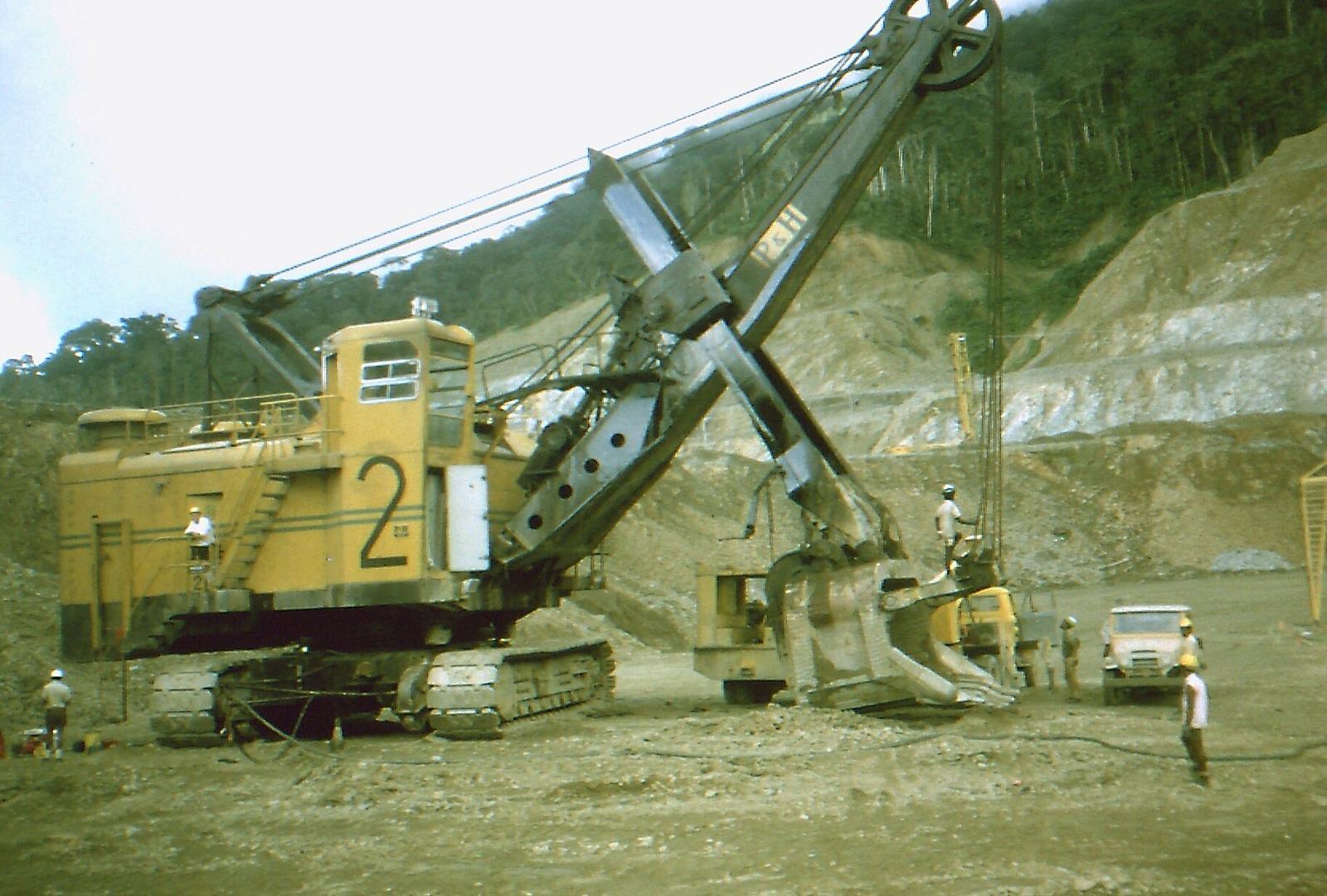 A large yellow electric shovel being serviced in a muddy pit, with workers around it